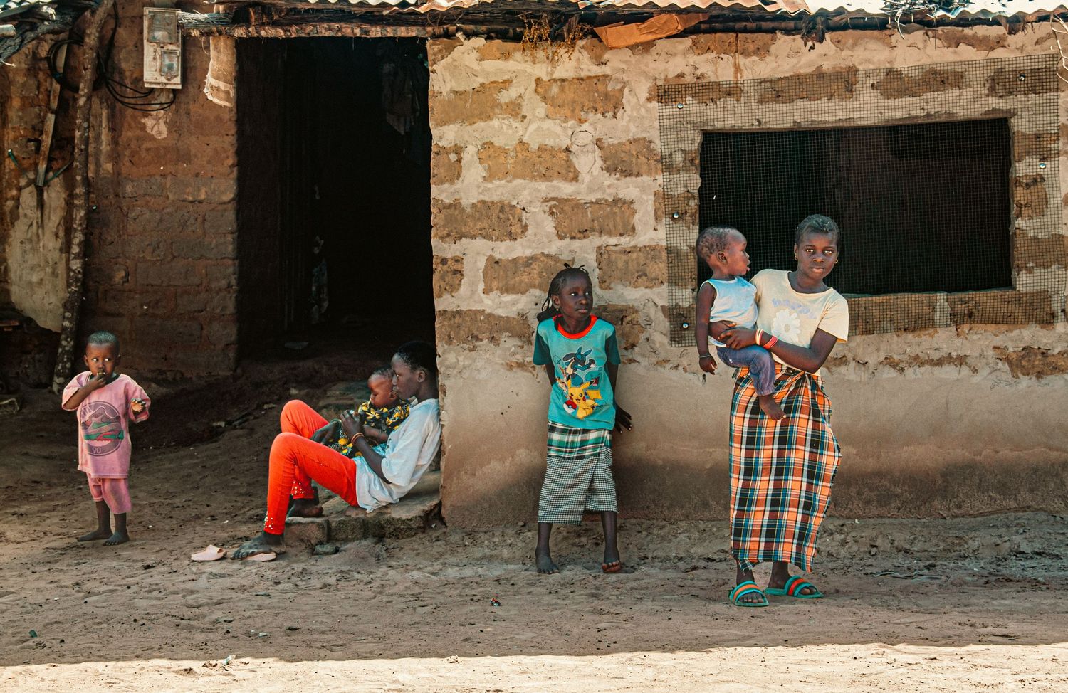 African family with children standing outside rustic stone brick building in rural village.