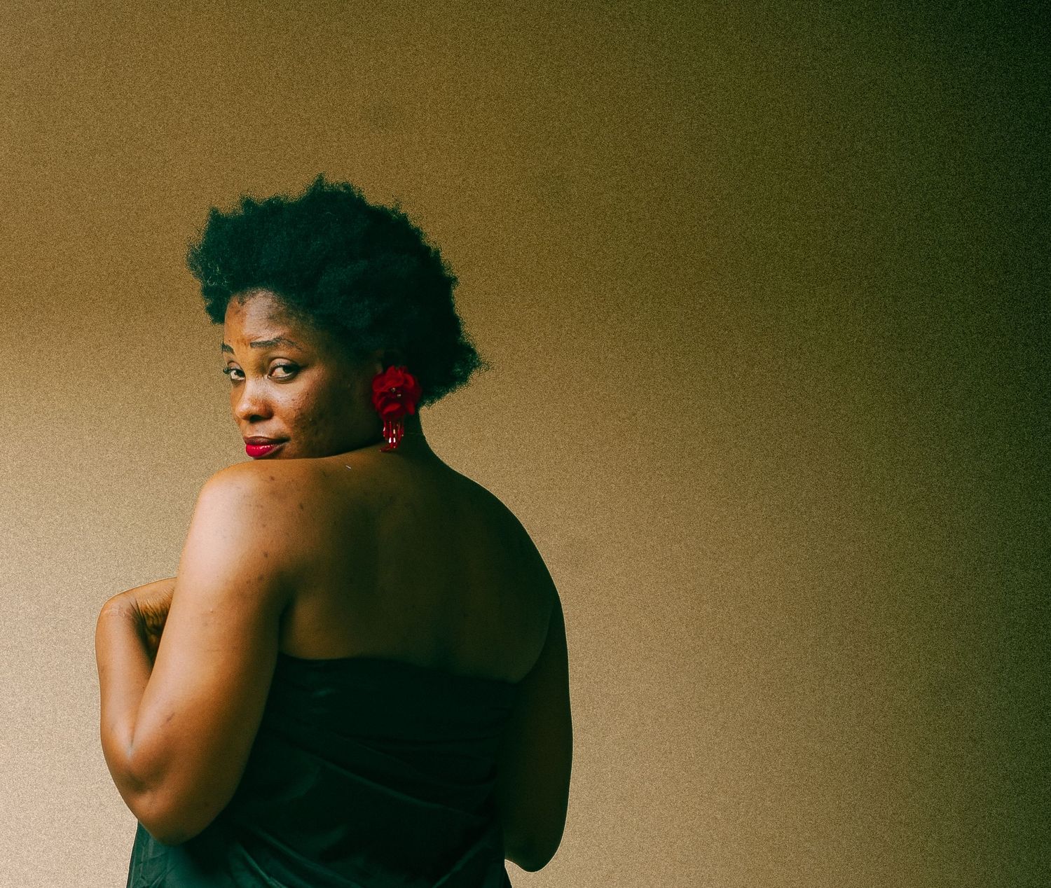 Black woman with natural hair and red earrings in green strapless dress looking over shoulder.