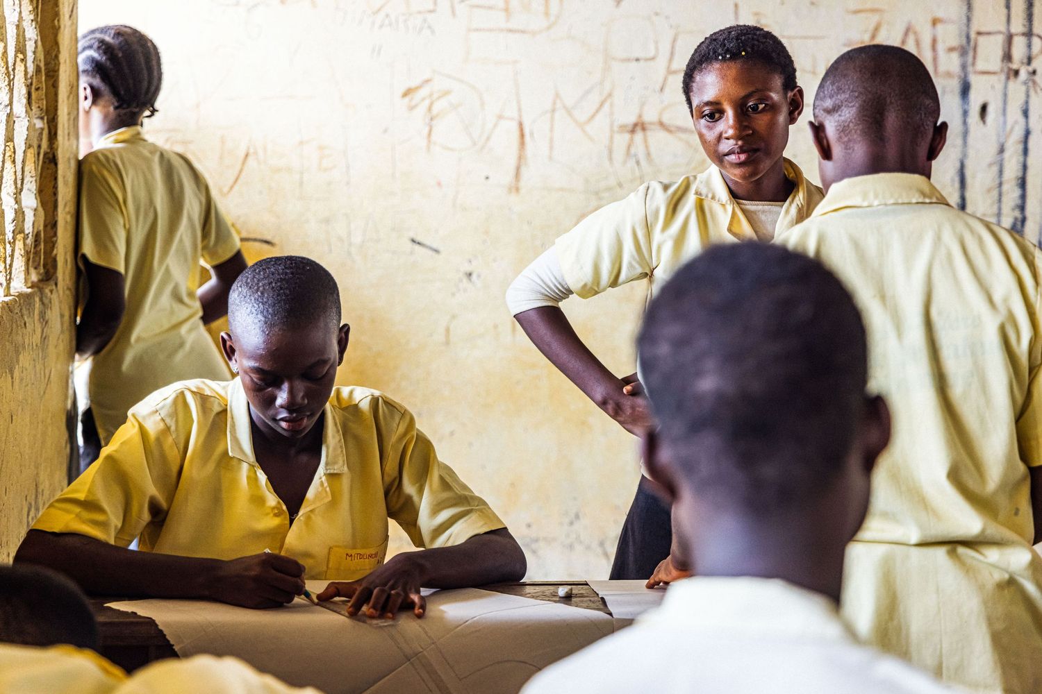 African students in yellow uniforms studying and interacting inside a rustic classroom.