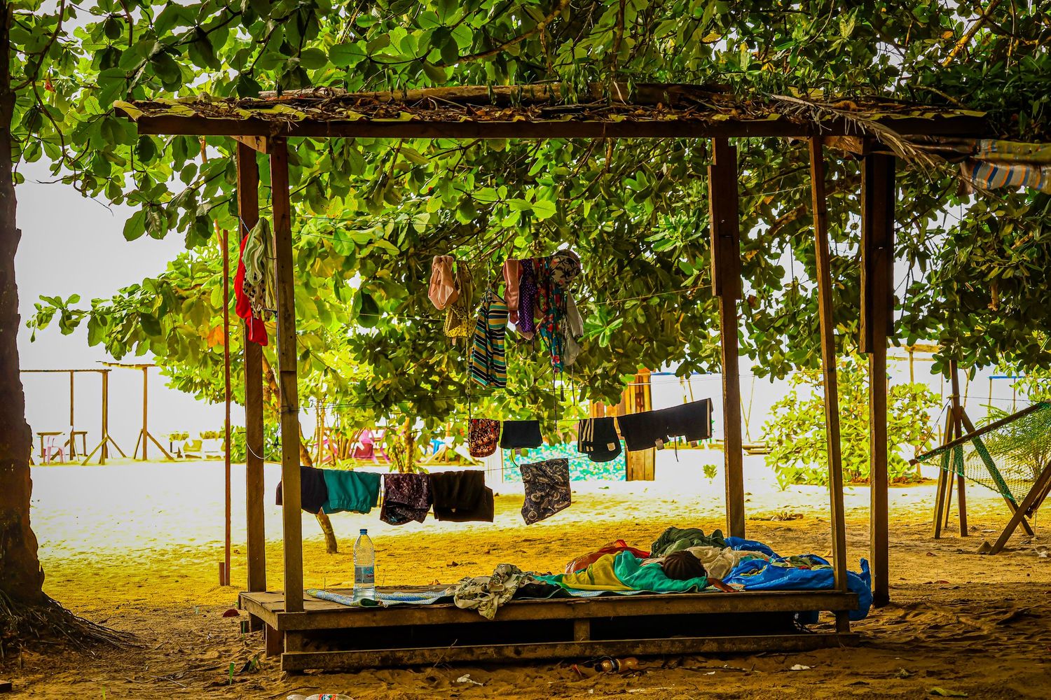 Colorful laundry hanging on a clothesline under a rustic wooden shelter near tropical trees.
