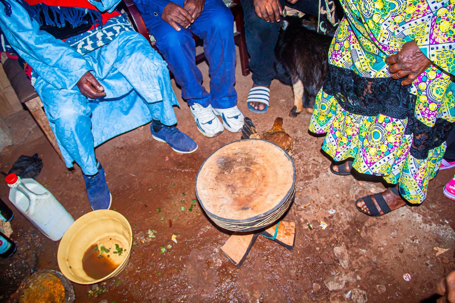 People in colorful African attire gathered around a large wooden drum during a traditional ceremony.