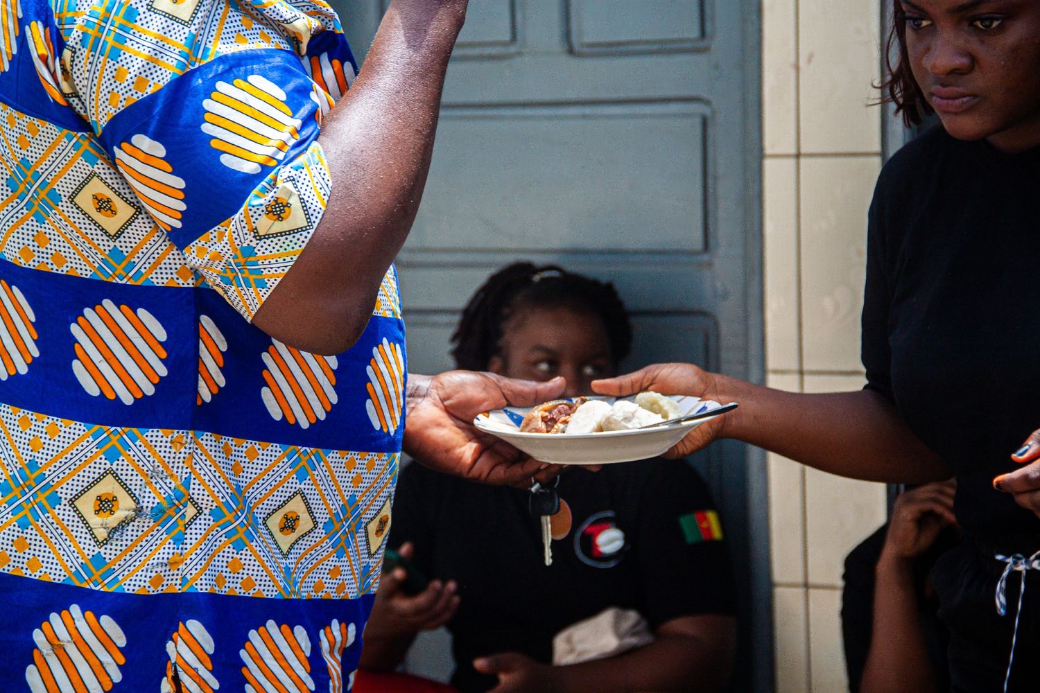 Woman in colorful African print dress serving food on a plate to another person.
