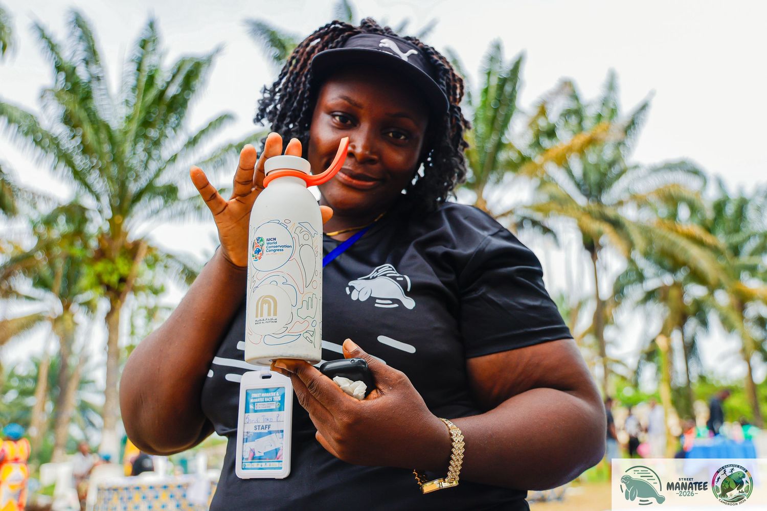 A woman proudly displays a branded water bottle at a tropical outdoor event with palm trees.