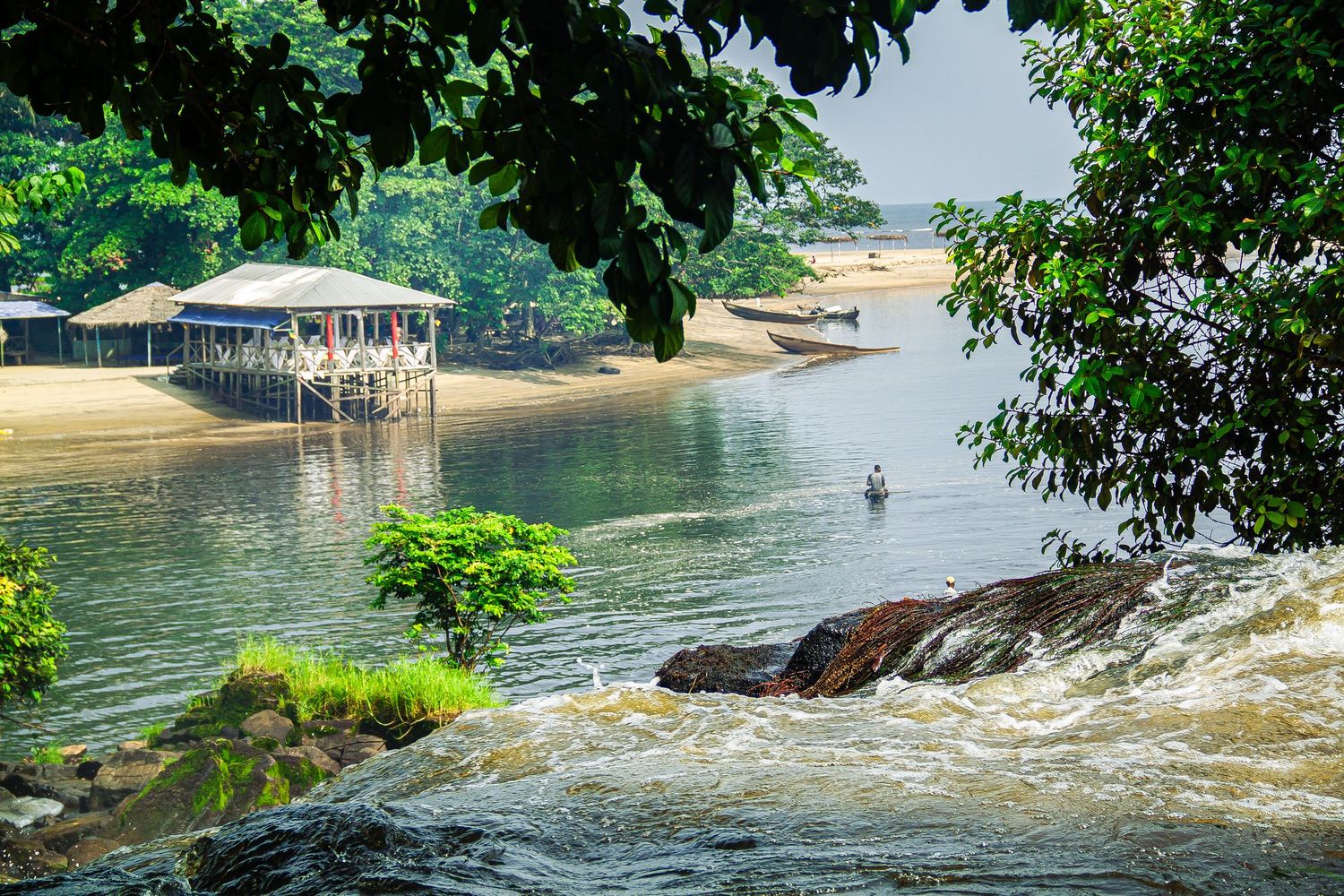 Scenic tropical river with rushing rapids flowing past sandy banks and lush green trees.