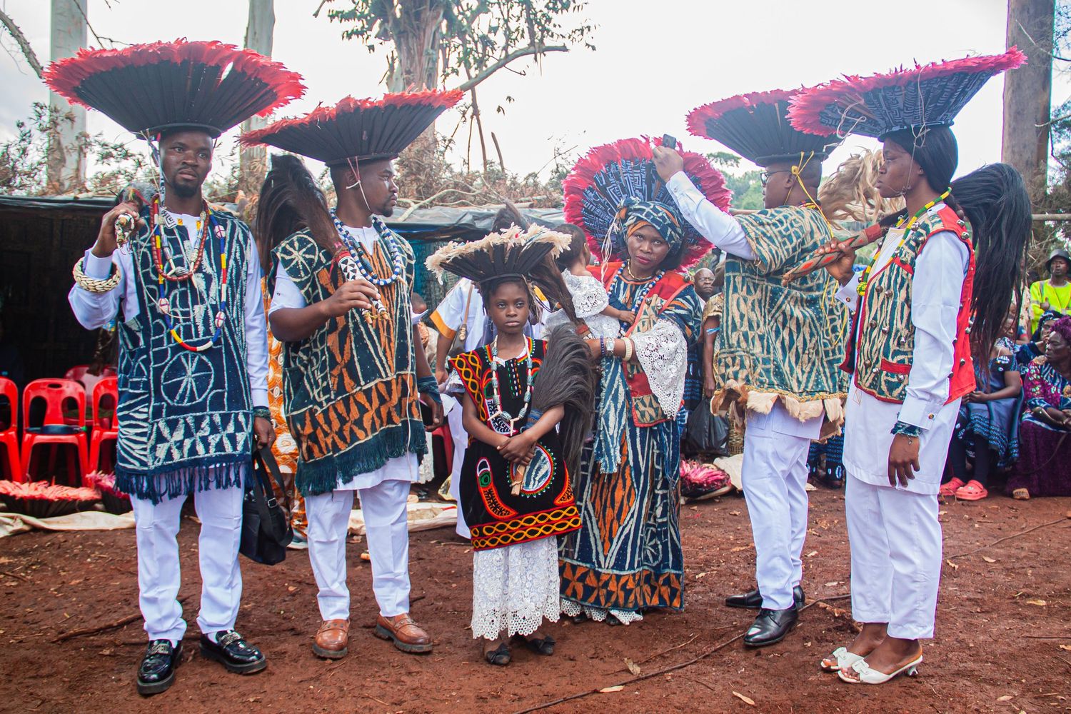 Colorfully dressed African performers in traditional attire with red feathered hats at a cultural ceremony.
