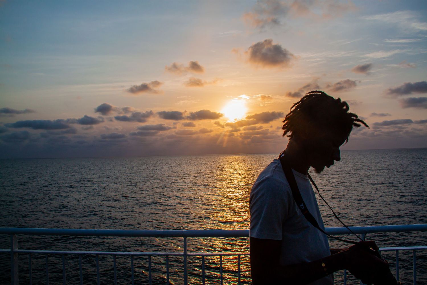 Silhouette of a person with dreadlocks standing on a deck at sunset over the ocean.