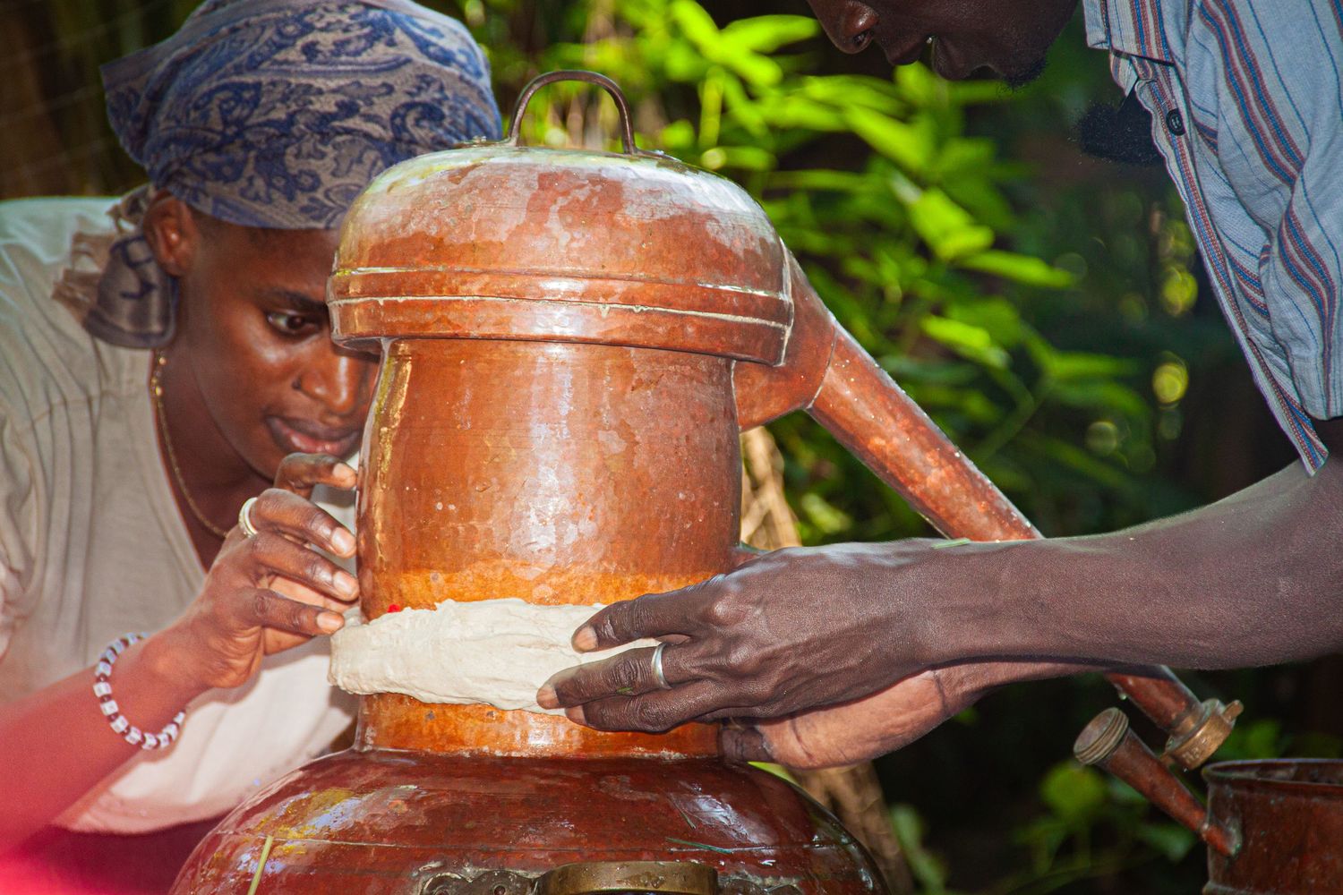 African woman closely inspecting food cooking in a large traditional clay pot outdoors.