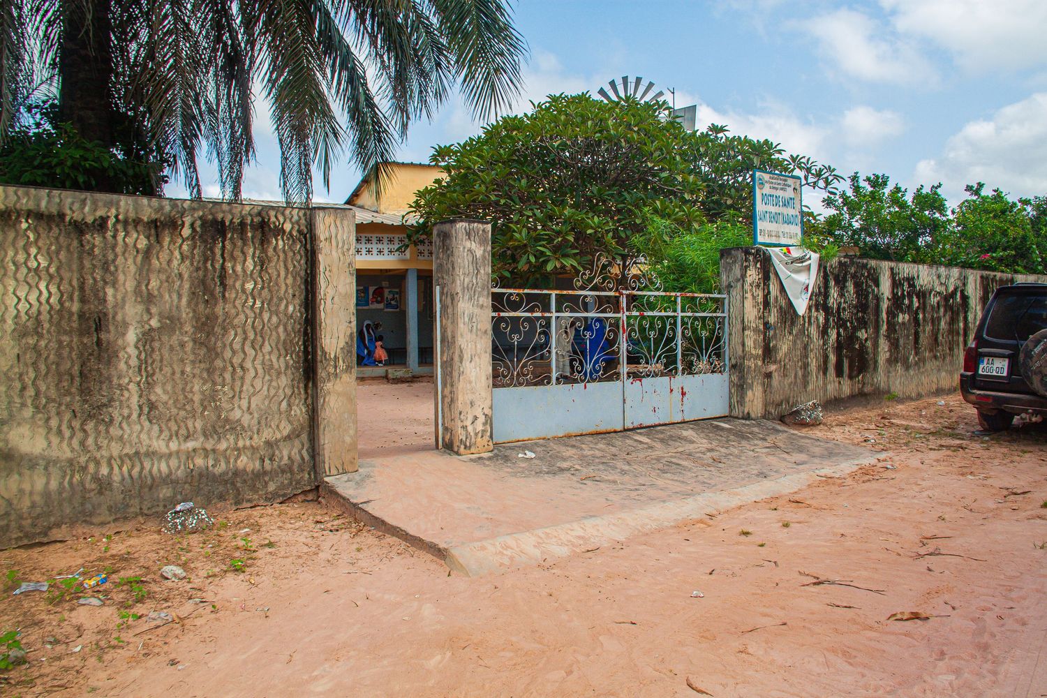 Entrance gate to a modest compound with blue metal fence on a red dirt road in Africa.