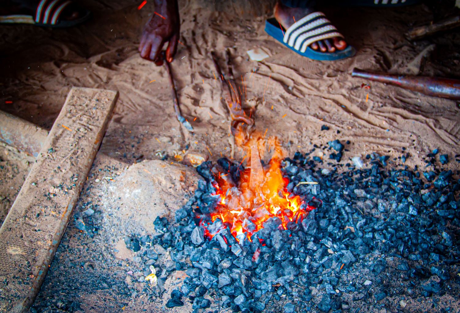 Bright orange flames burning in charcoal embers at a traditional African blacksmith forge.