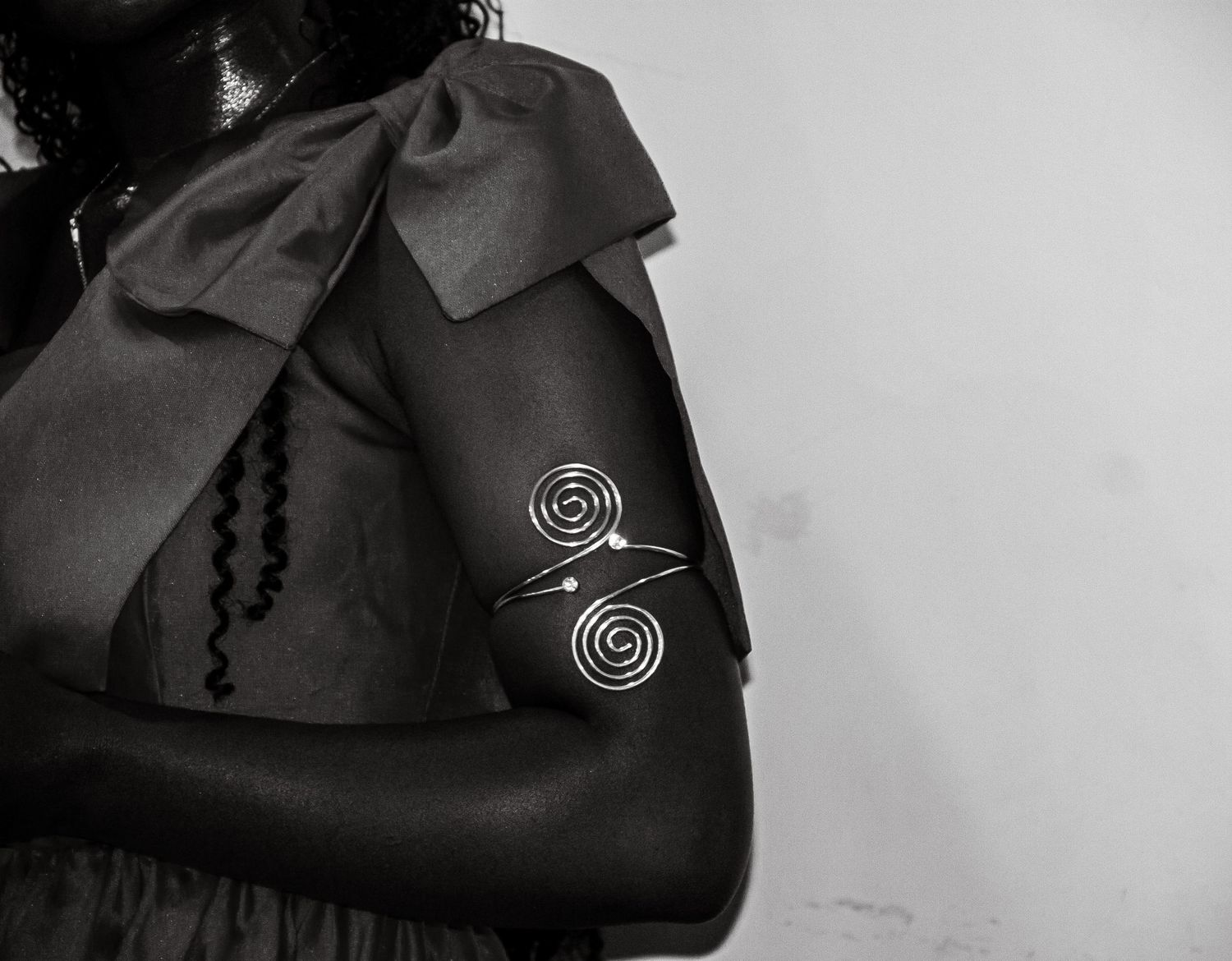 Black and white close-up of decorative silver spiral arm cuff bracelet on a woman.