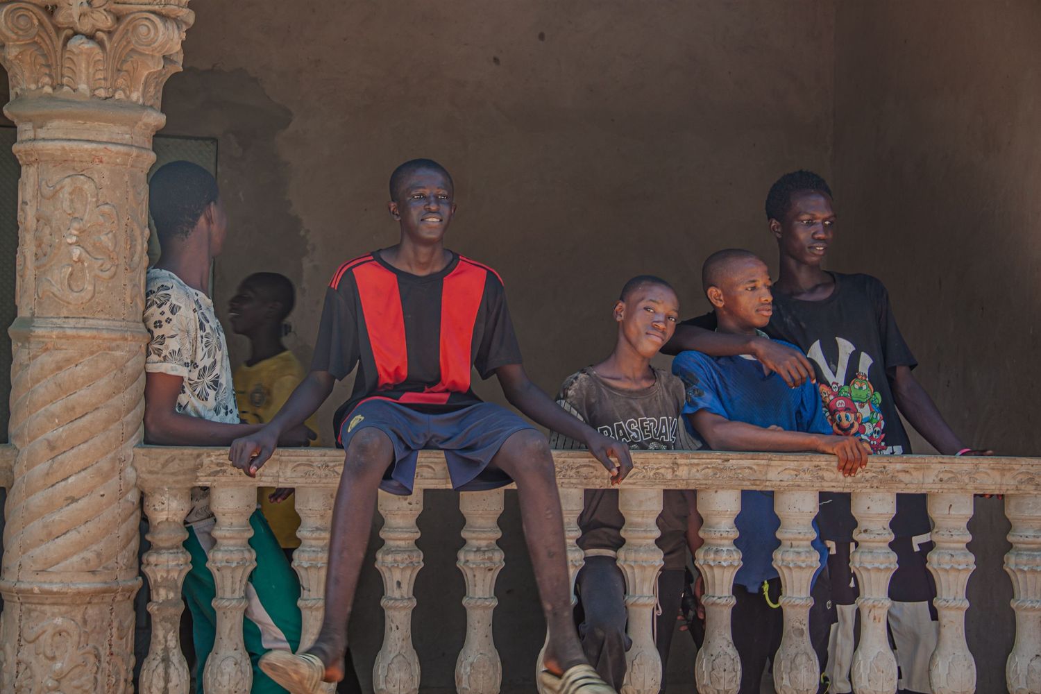 Group of young African boys relaxing on a decorative balcony railing of a traditional building.