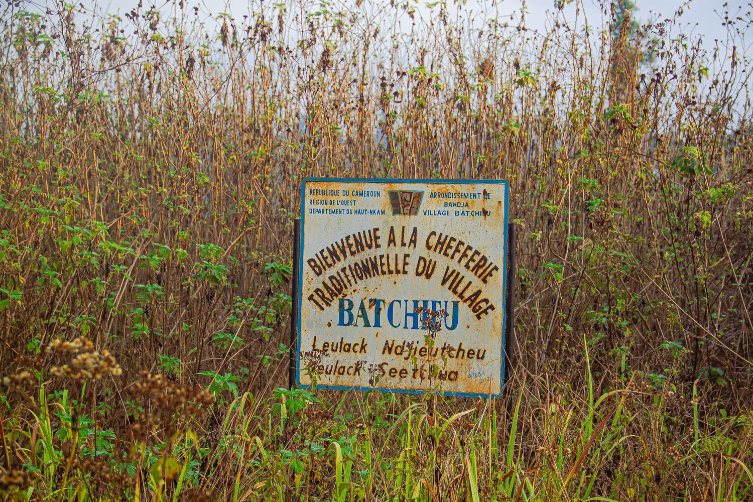 Welcome sign for Batcheu traditional village chiefdom surrounded by tall dry grass in Cameroon.