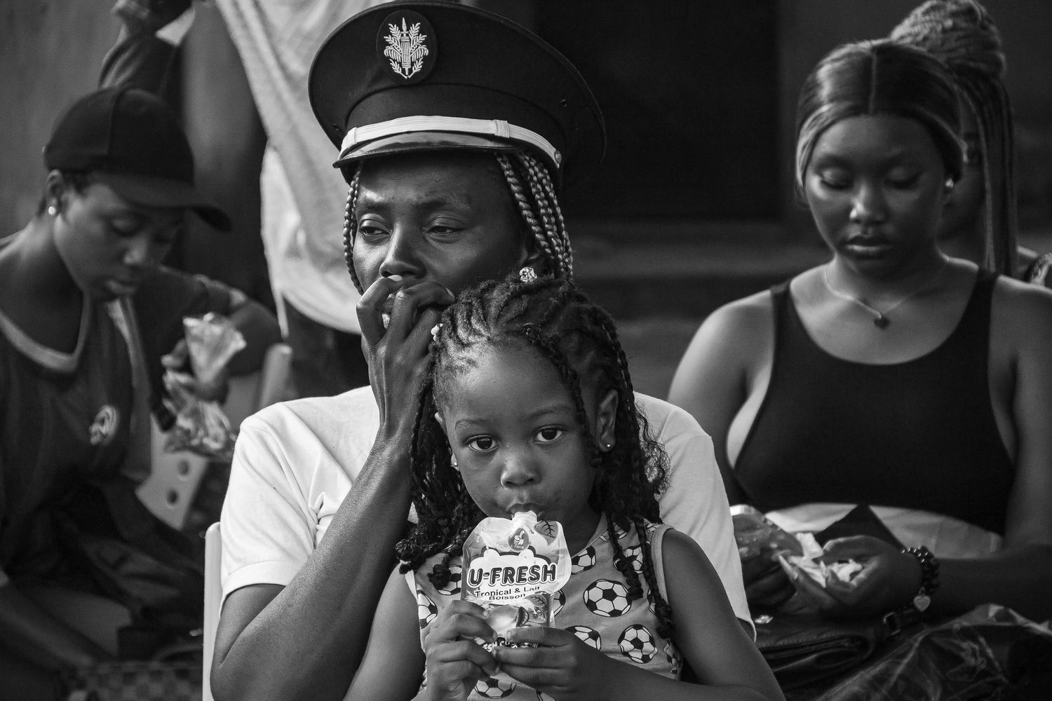 Black and white photo of a man wearing a military cap holding a young girl eating ice cream at a gathering.
