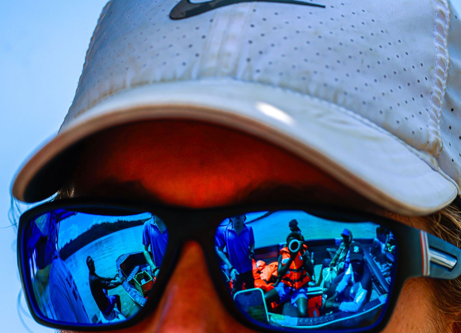 A close-up of a man in sunglasses reflecting a boat scene on a sunny day.