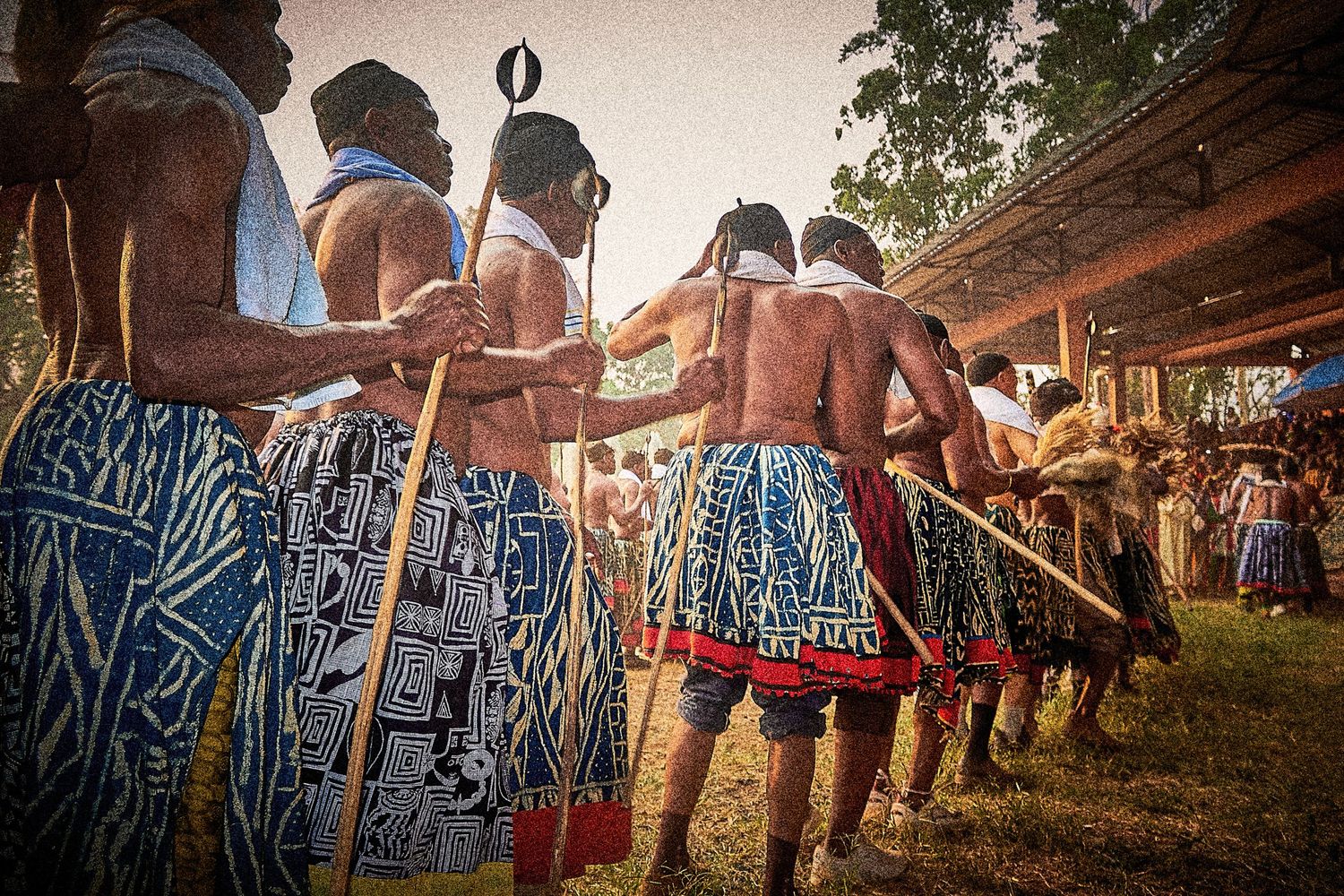 Traditional African dancers in colorful patterned skirts holding spears during cultural ceremony.
