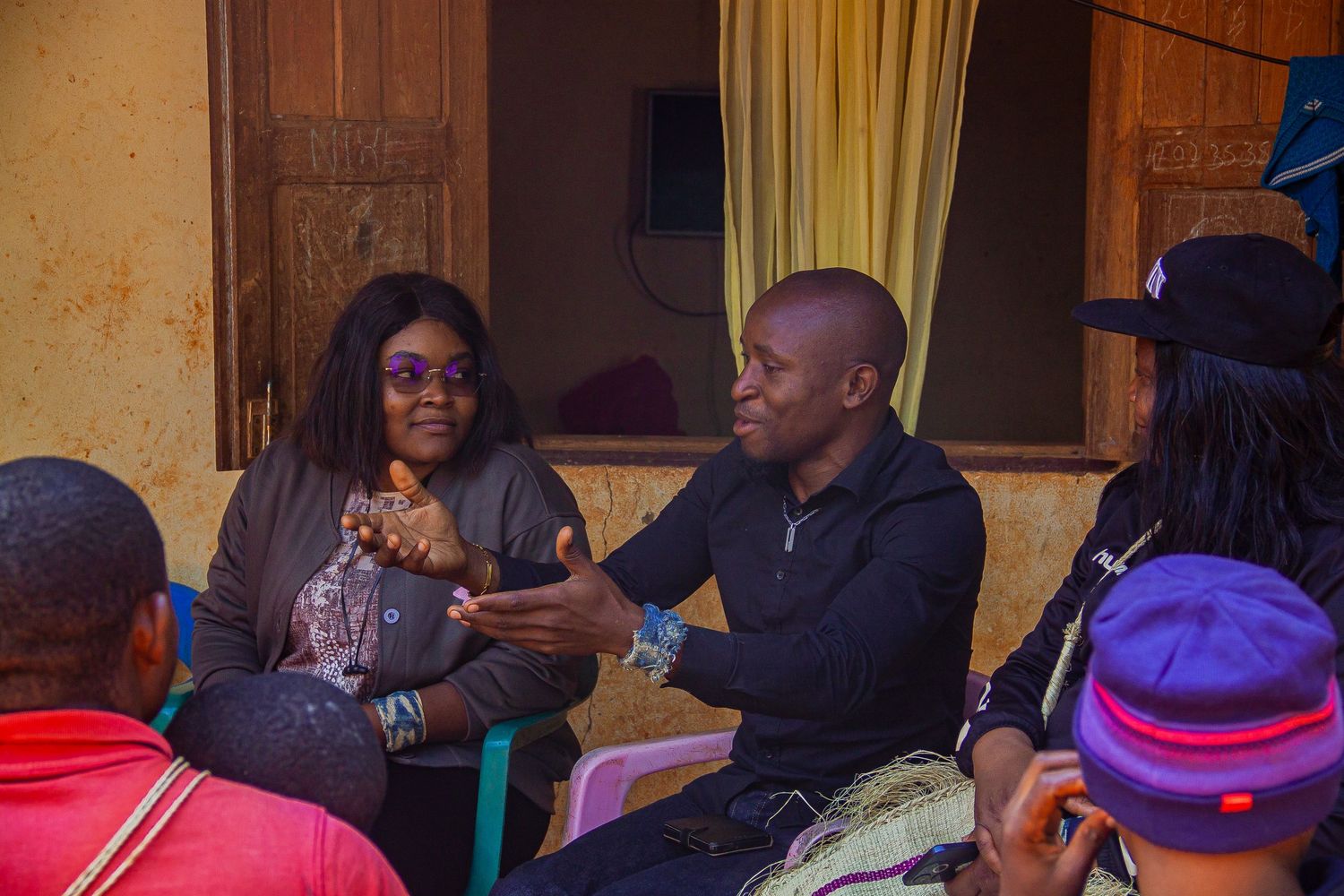Group of African adults engaged in conversation while seated in casual outdoor gathering.