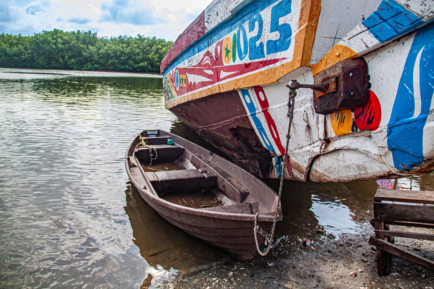 Colorful wooden fishing boats moored along a calm river surrounded by lush mangroves.