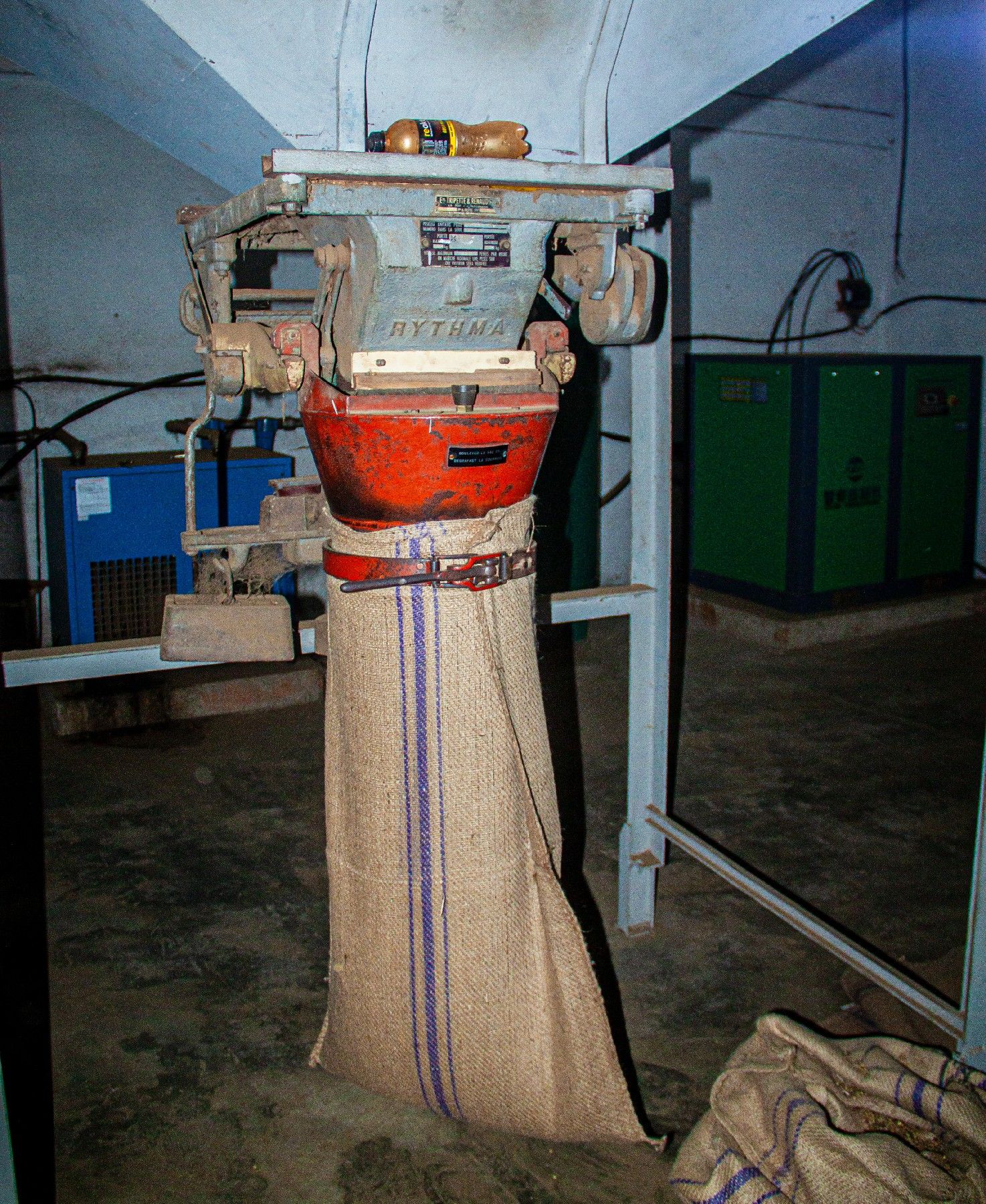 Industrial burlap sack filling machine in a dimly lit warehouse processing facility.