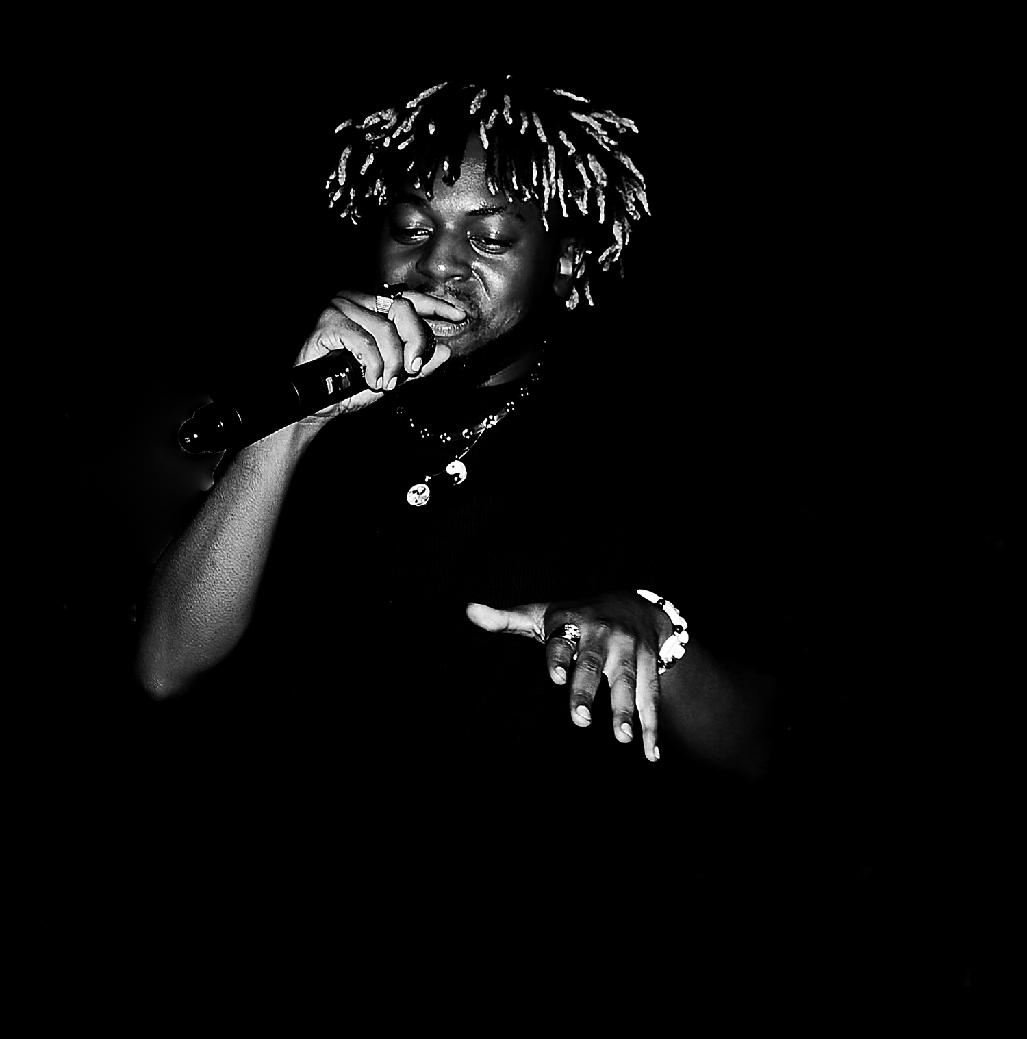 Black and white dramatic photo of an African artist performing with a microphone in low stage lighting.