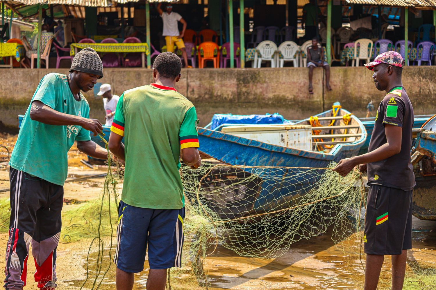 Three African fishermen working together to manage fishing nets beside a blue boat.