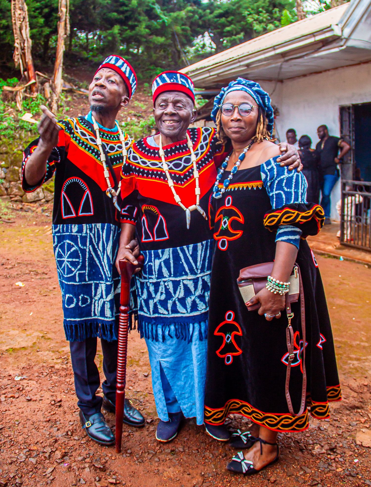 Three people in colorful traditional Cameroonian Ndop attire posing together at an outdoor event.