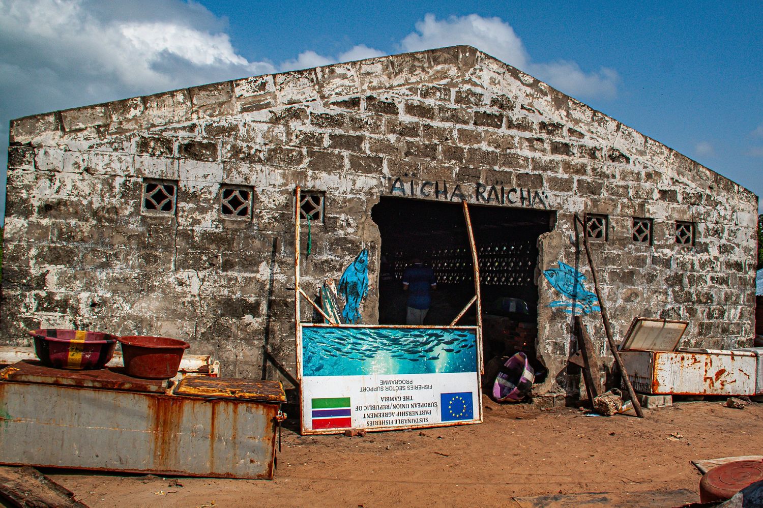Weathered stone building with EU-funded project signage in a West African coastal town.