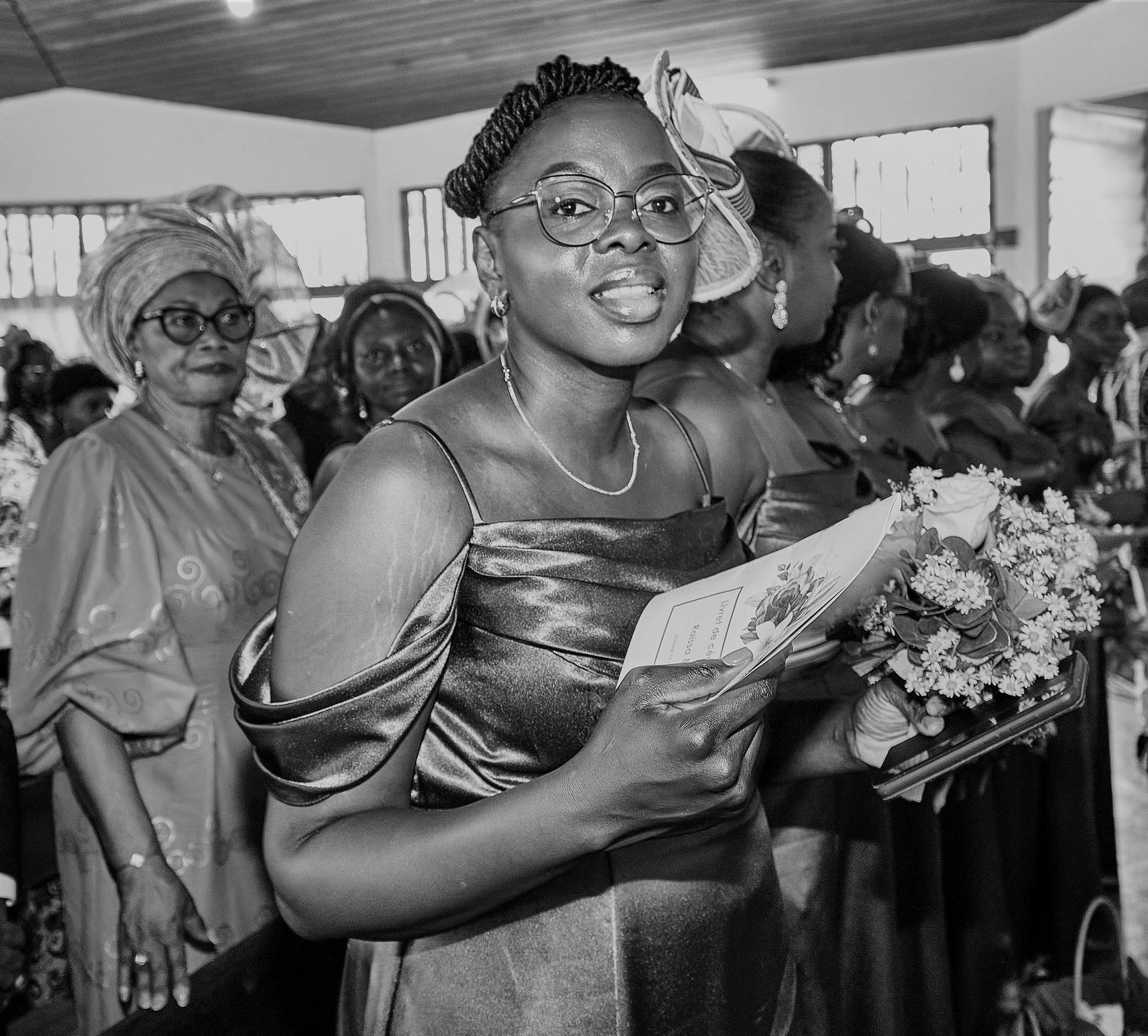 Smiling woman in a satin dress holding flowers at a formal indoor celebration.
