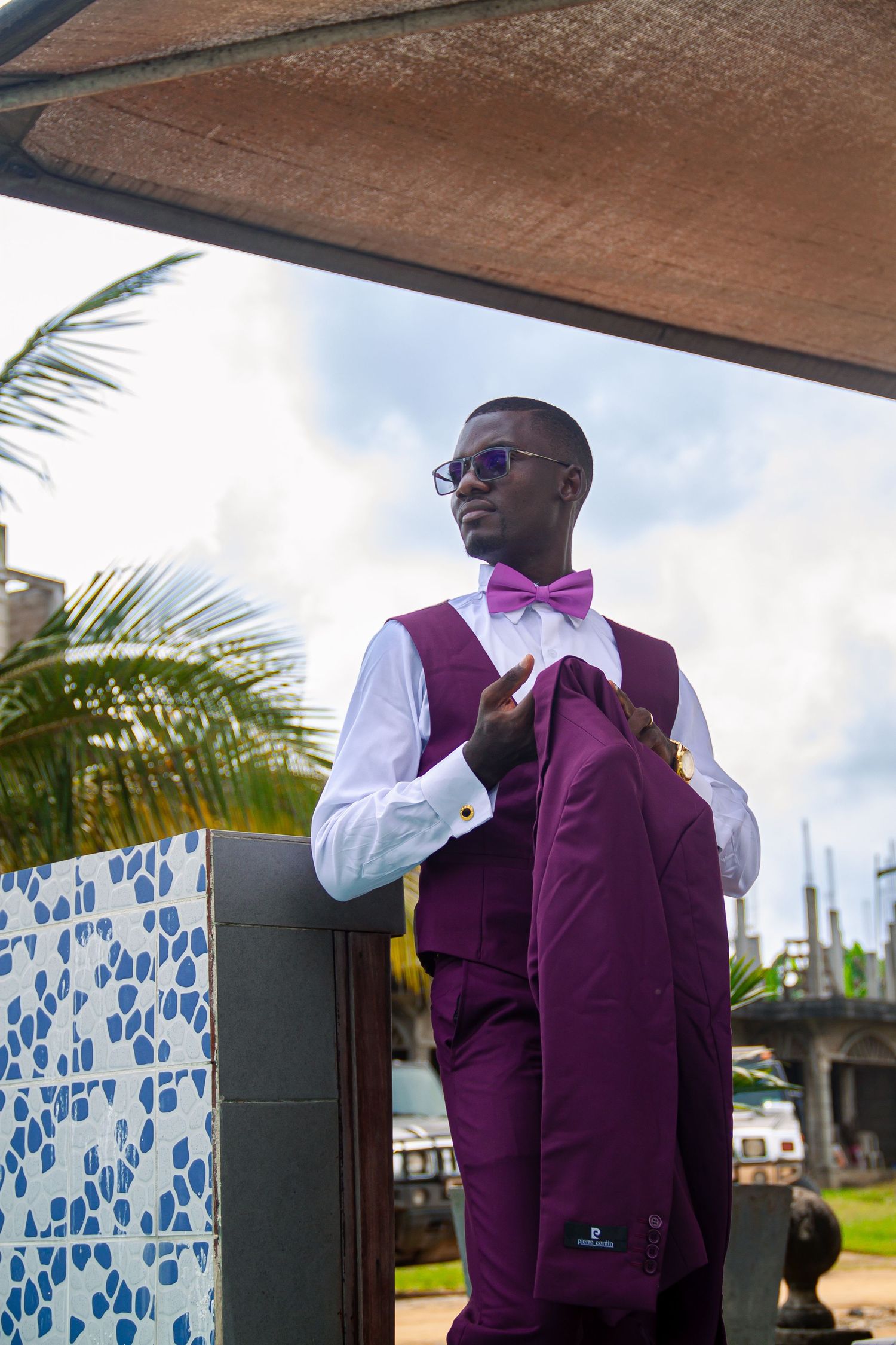 Elegant man in purple vest and bow tie holding jacket at outdoor venue.