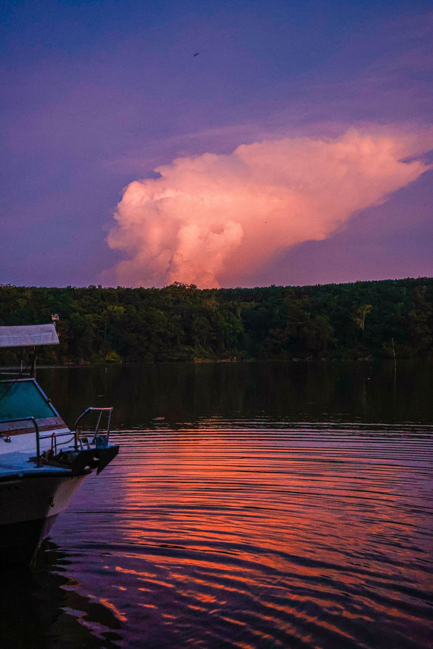 Dramatic pink and purple sunset over a river with a large storm cloud and docked boat.