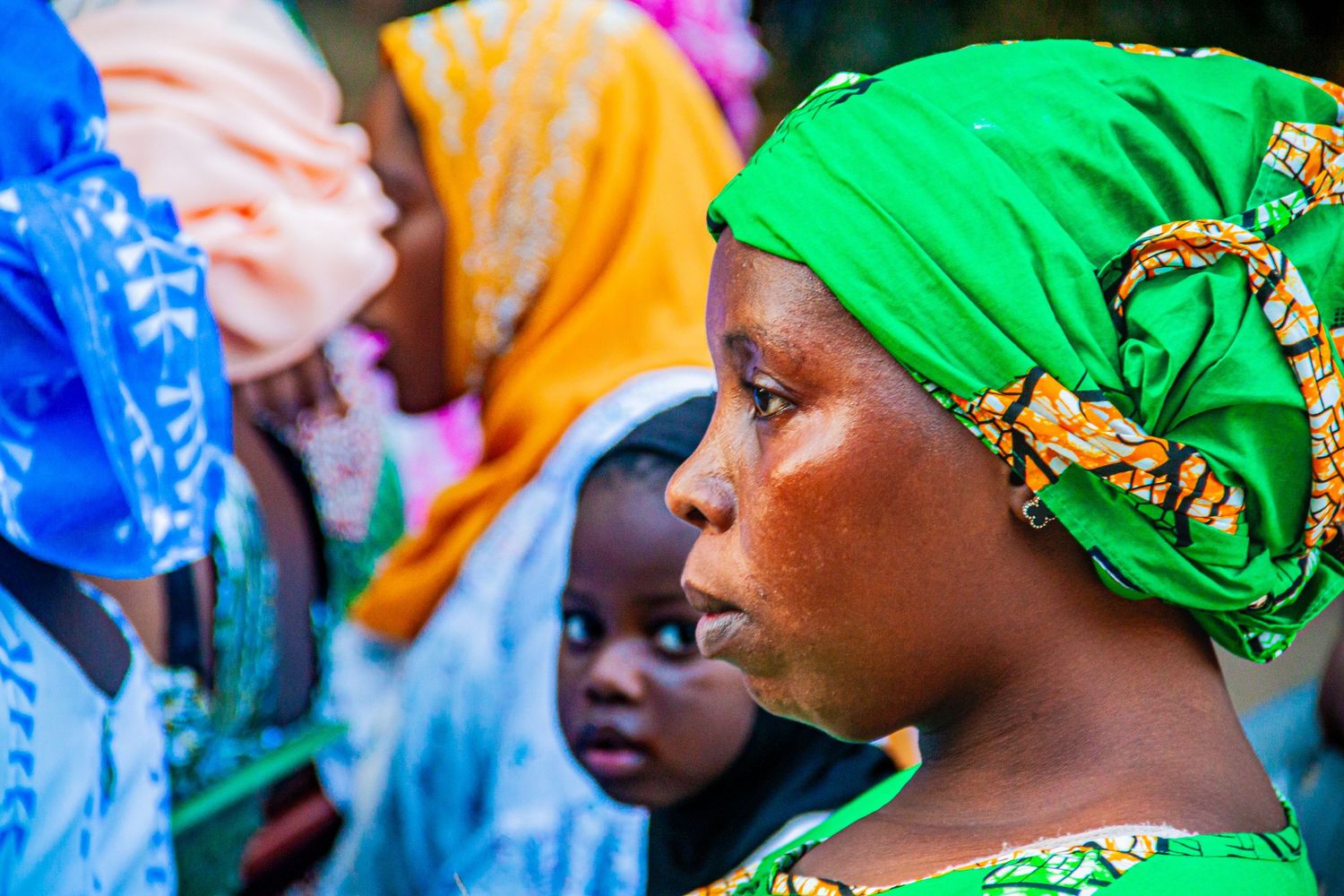 African women wearing colorful hijabs and headscarves gathered together in a community setting.