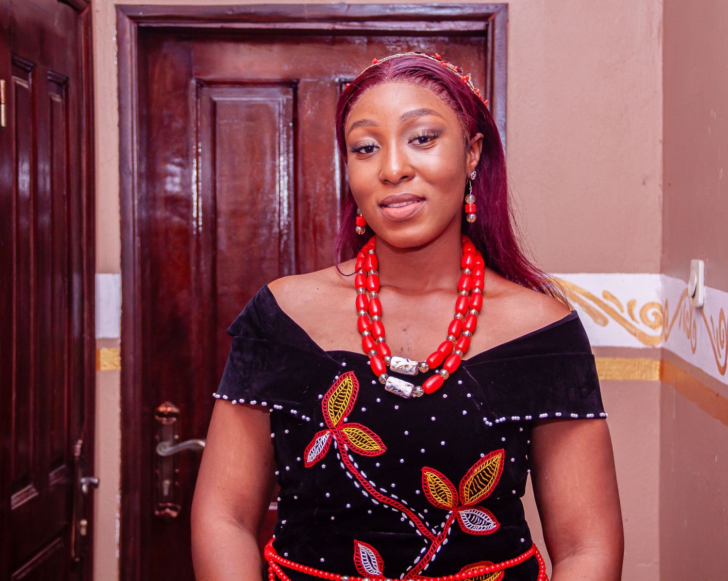 African woman in traditional black and red embroidered attire with red beaded jewelry.
