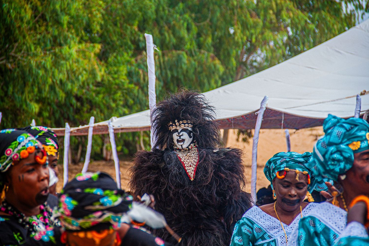 A performer in a black feathered mask and costume at a traditional African festival.