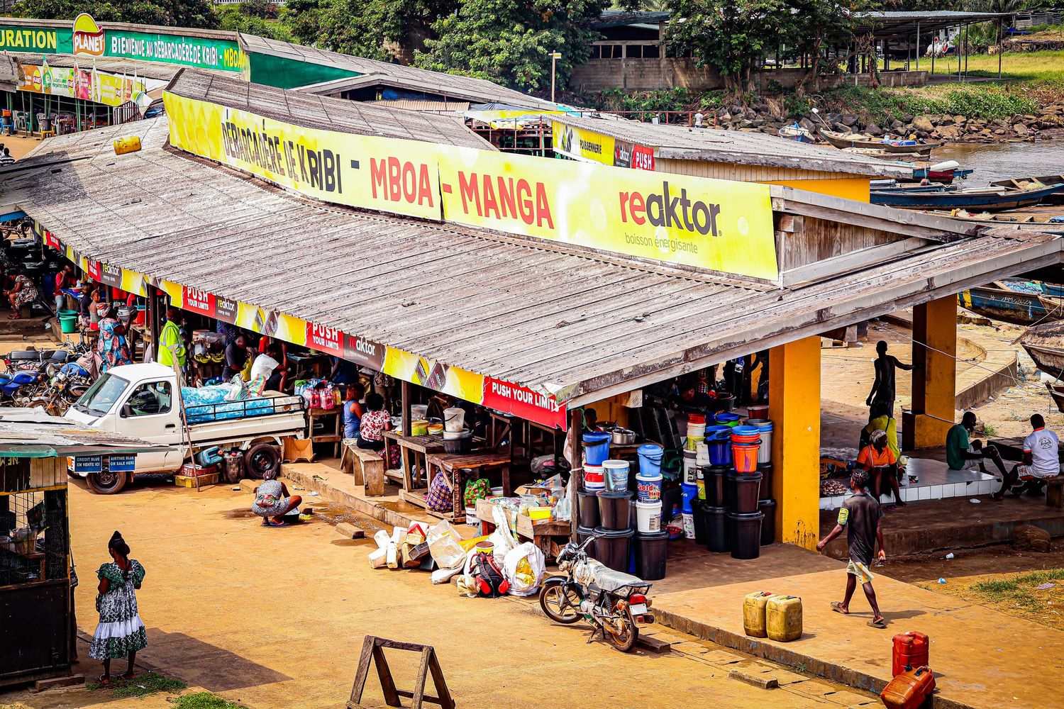 Busy African market street with colorful shop signs and vendors in a dusty town.