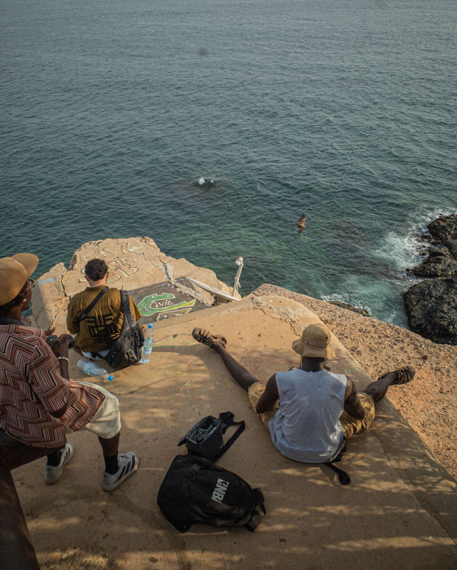 Group of people sitting on rocky cliff overlooking the turquoise ocean waters in Senegal, Africa.