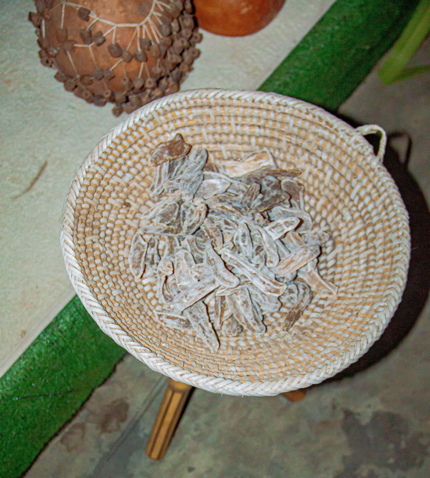 Dried herb fragments in a handwoven white basket on a wooden stool with green carpet background.