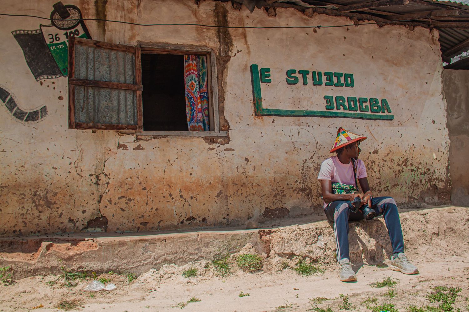 Man sitting outside a rustic studio building in a small African village.