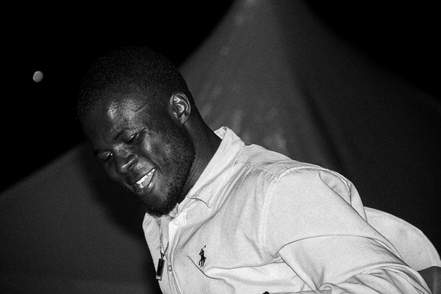 Black and white portrait of a man in a polo shirt looking down, dramatic lighting.