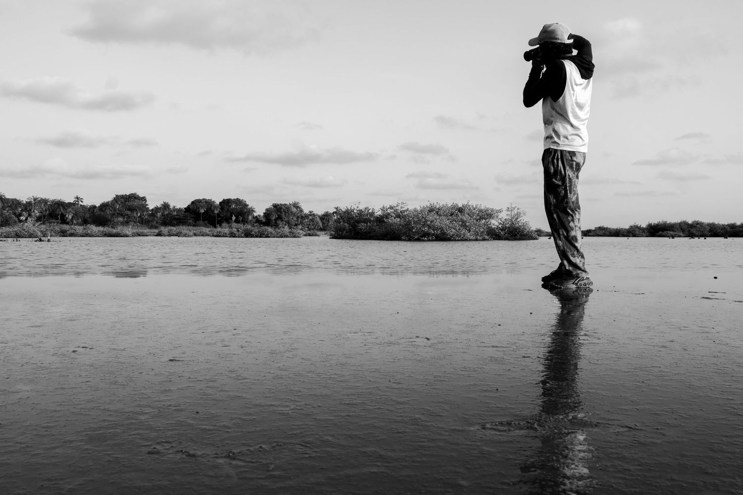 A photographer stands in shallow water capturing landscape shots in a black and white nature scene.