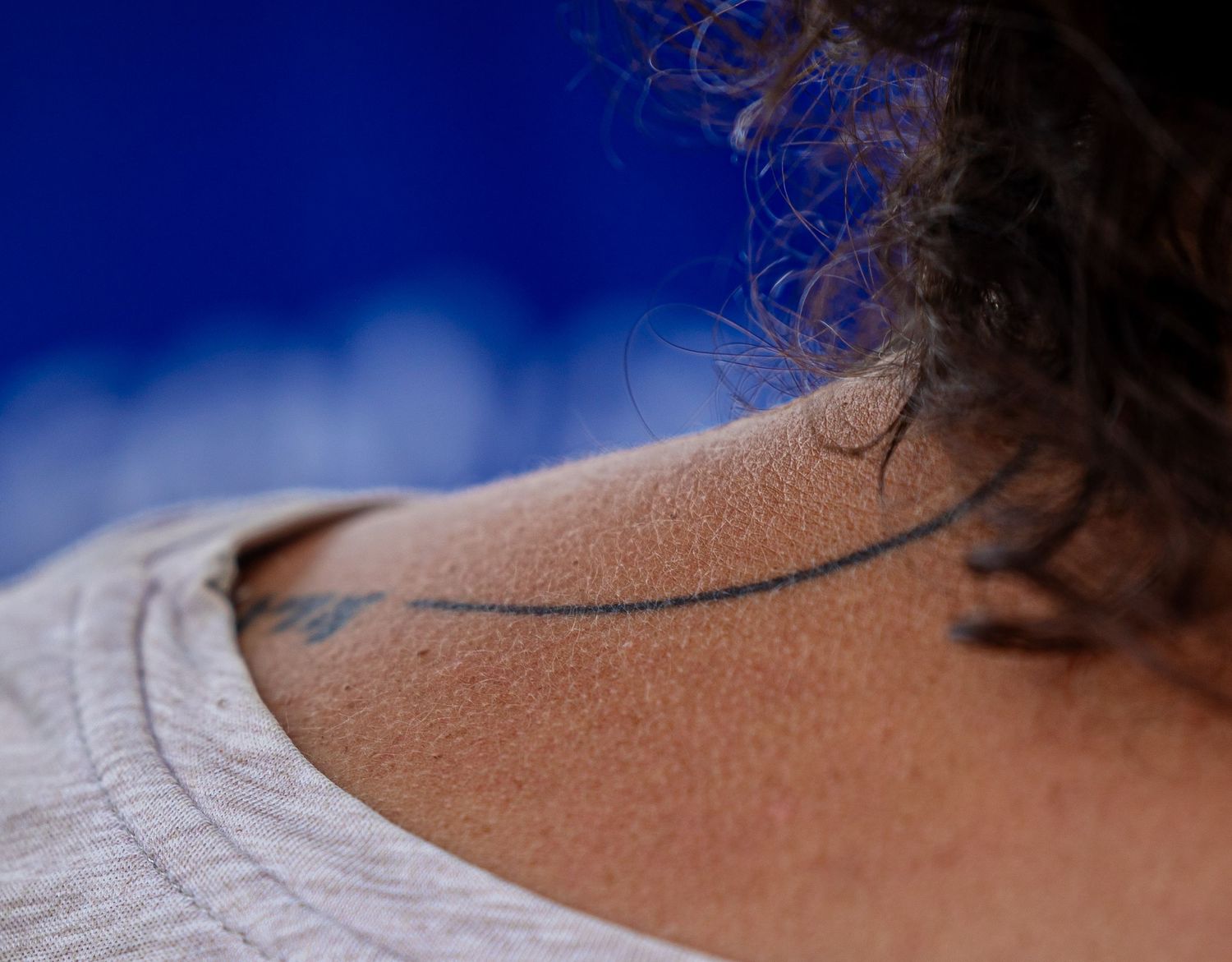 Close-up of a tattoo on a person's shoulder with curly hair against a blue background.