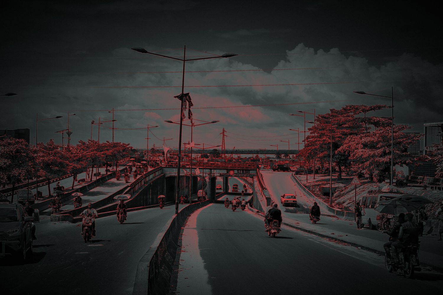 Dark moody urban street scene with red-tinted trees and busy underpass in an African city.