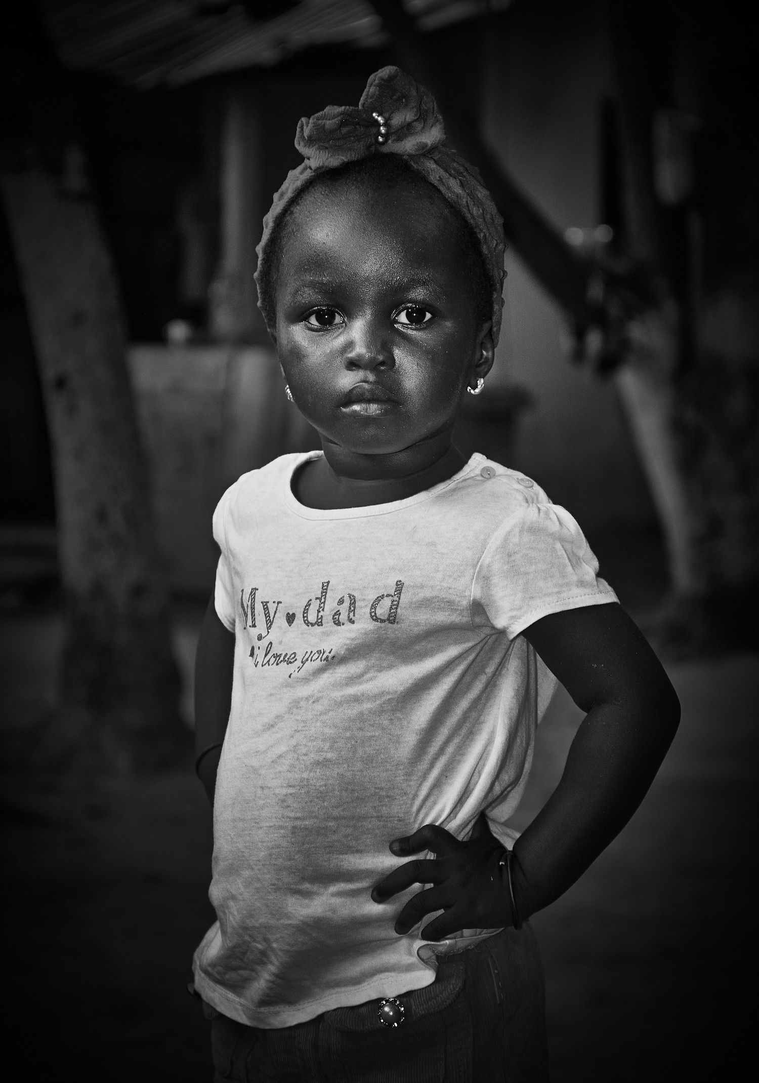 Young African girl in white My Dad t-shirt posing confidently in black and white photo.