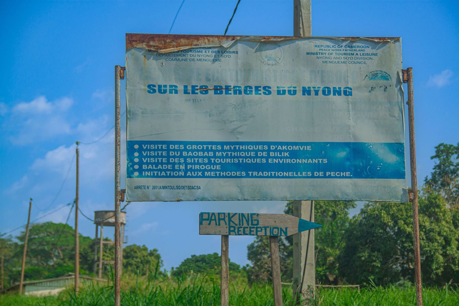 French tourism sign for Sur Les Berges Du Nyong with parking directions in a lush green African landscape.