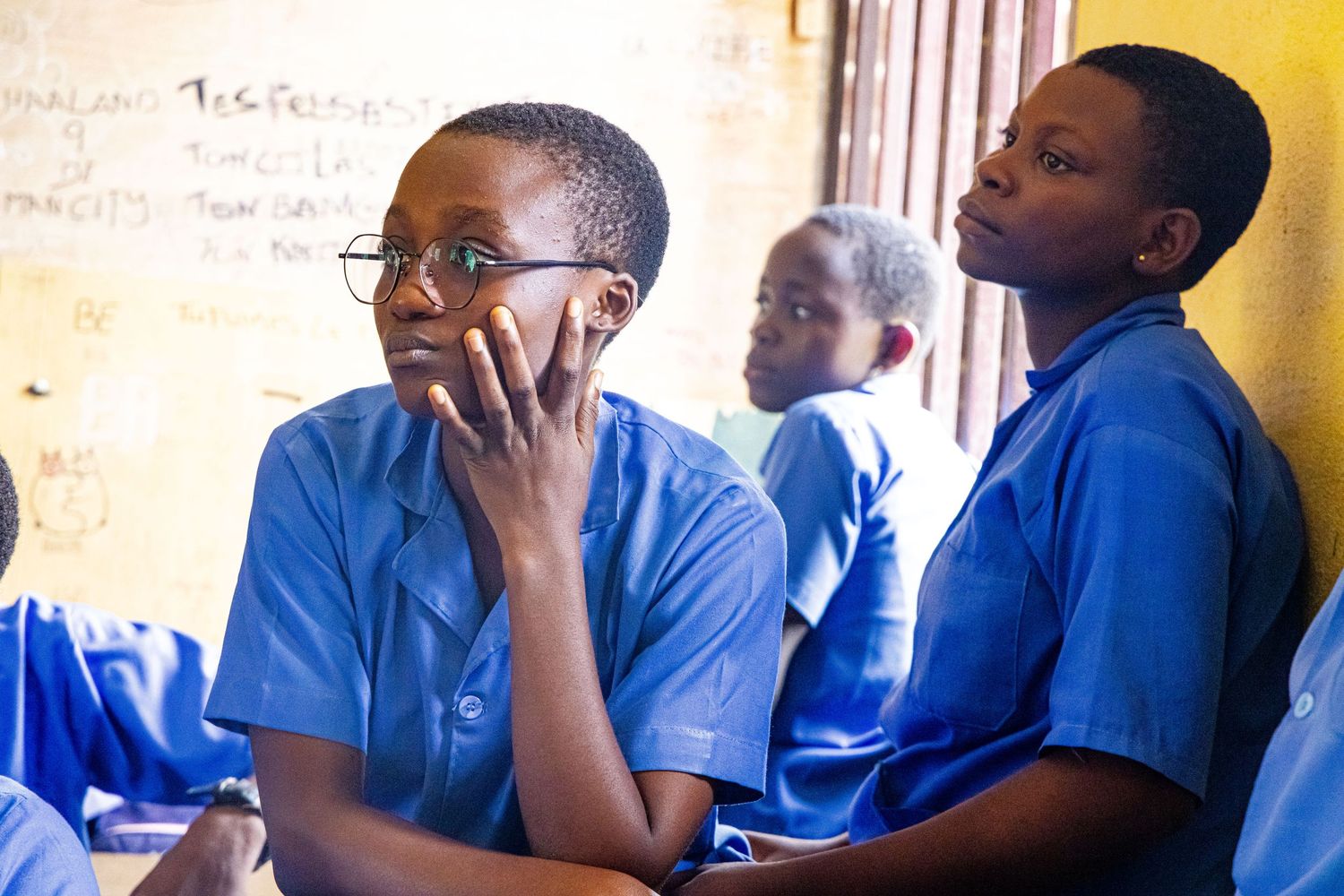 Two African students in blue uniforms sitting attentively in a classroom setting.