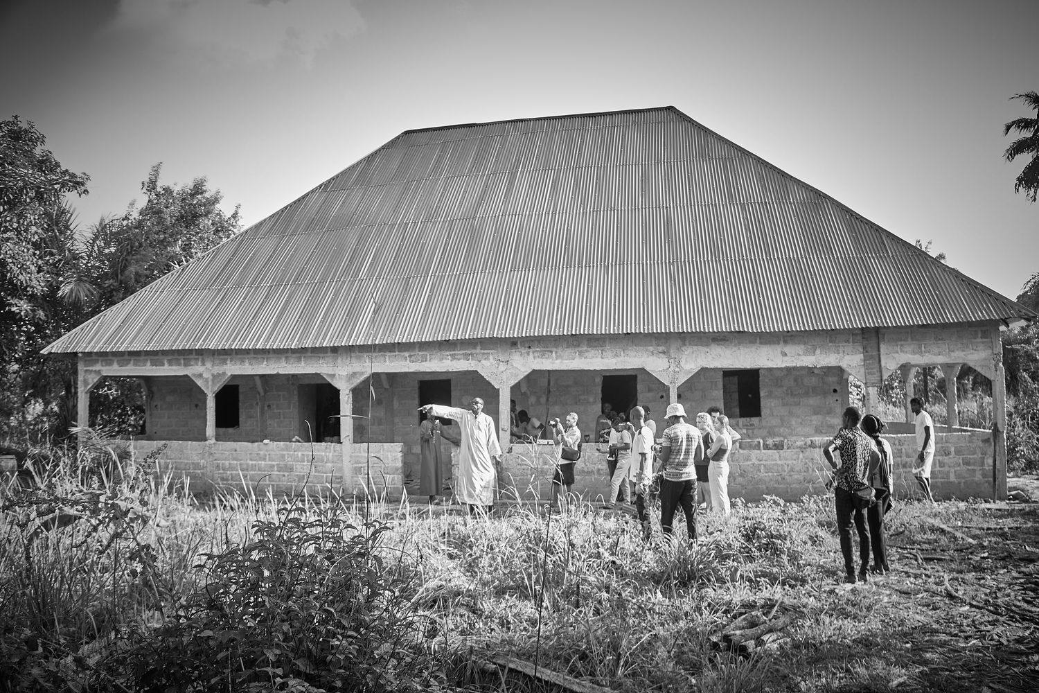 Black and white photo of a large metal-roofed building surrounded by people in a rural African setting.