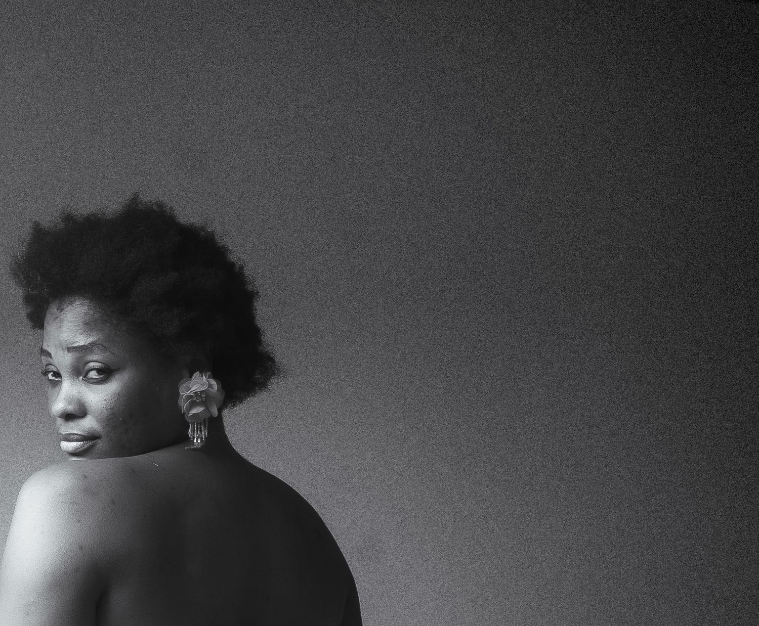Black and white portrait of woman with natural afro hair and earring looking over bare shoulder.