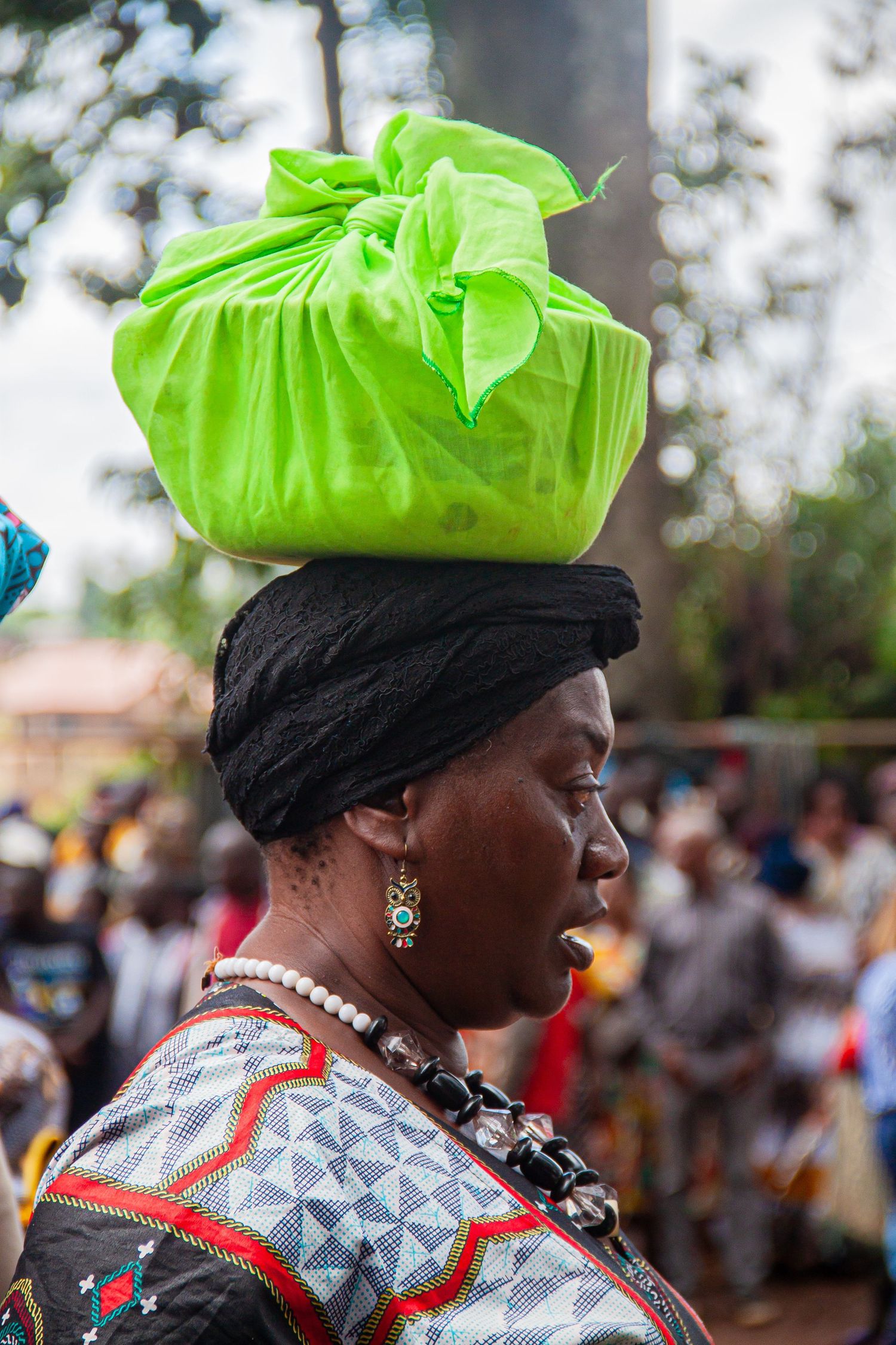African woman balancing bright green fabric bundle on head at traditional cultural gathering.