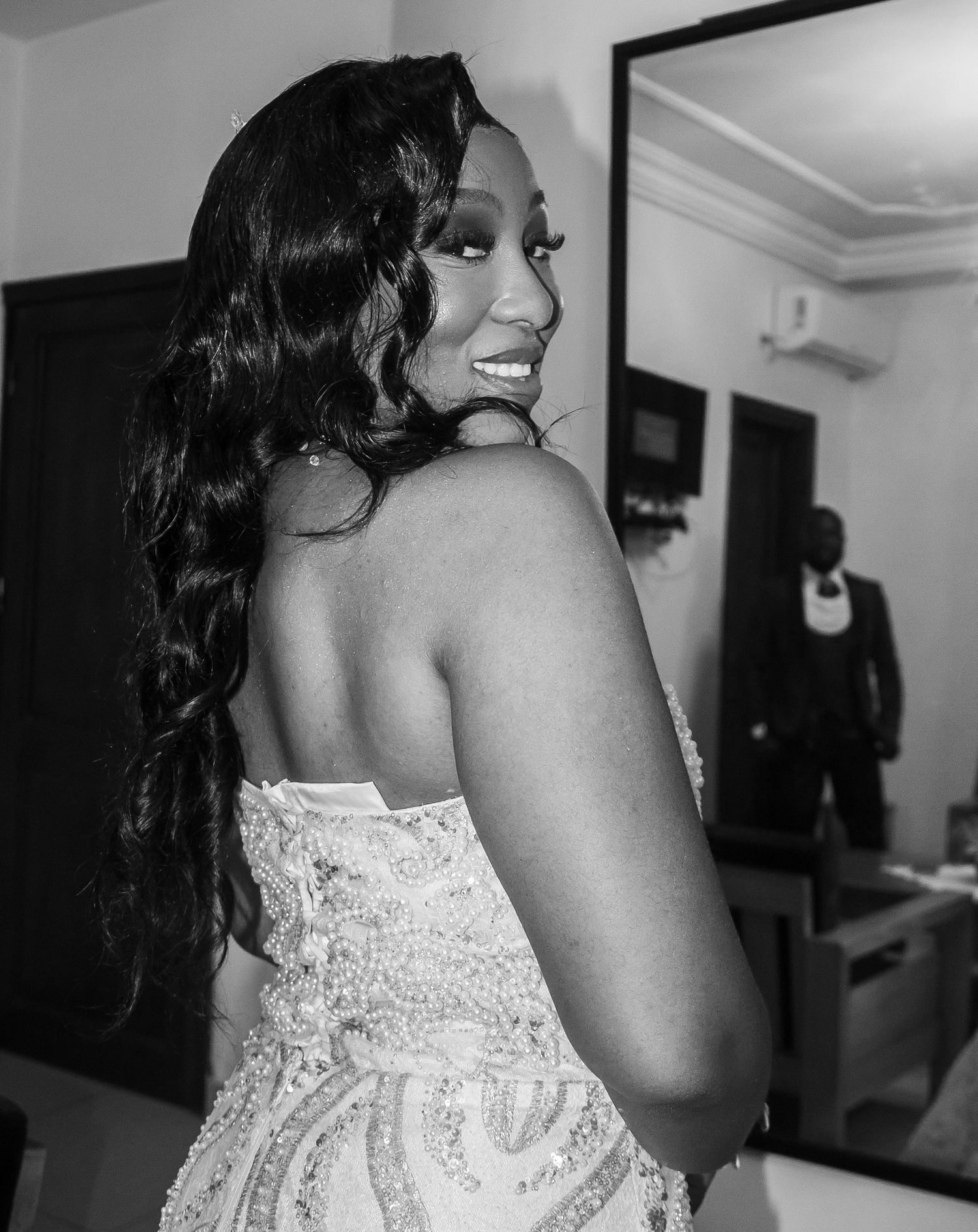 Black and white portrait of bride in beaded gown looking over shoulder, smiling.