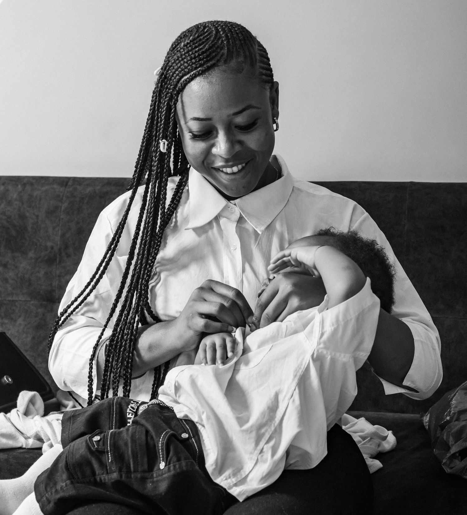 Black and white photo of smiling woman with braids breastfeeding baby on sofa.
