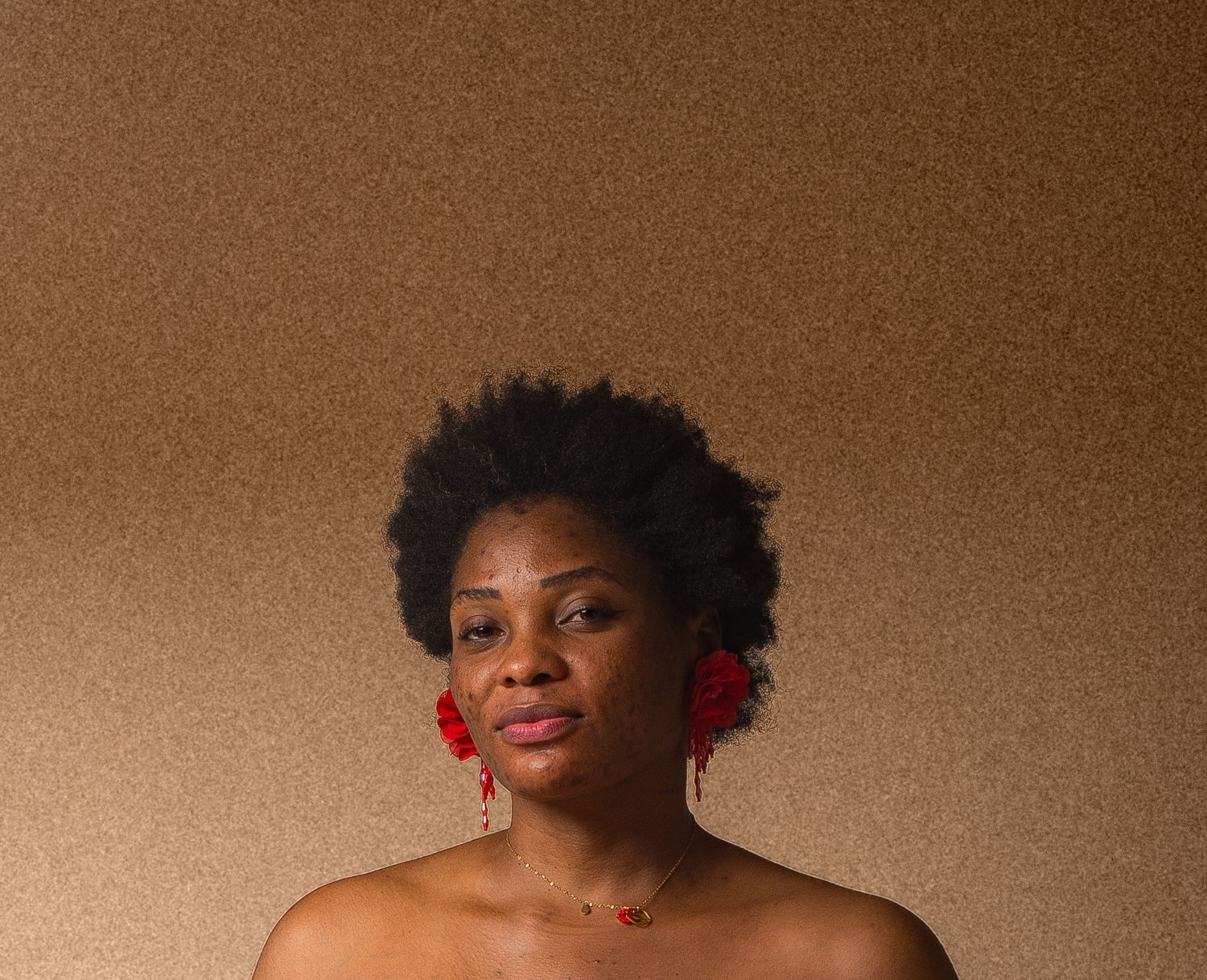 Black woman with natural afro hair and red floral earrings gazing upward against brown background.