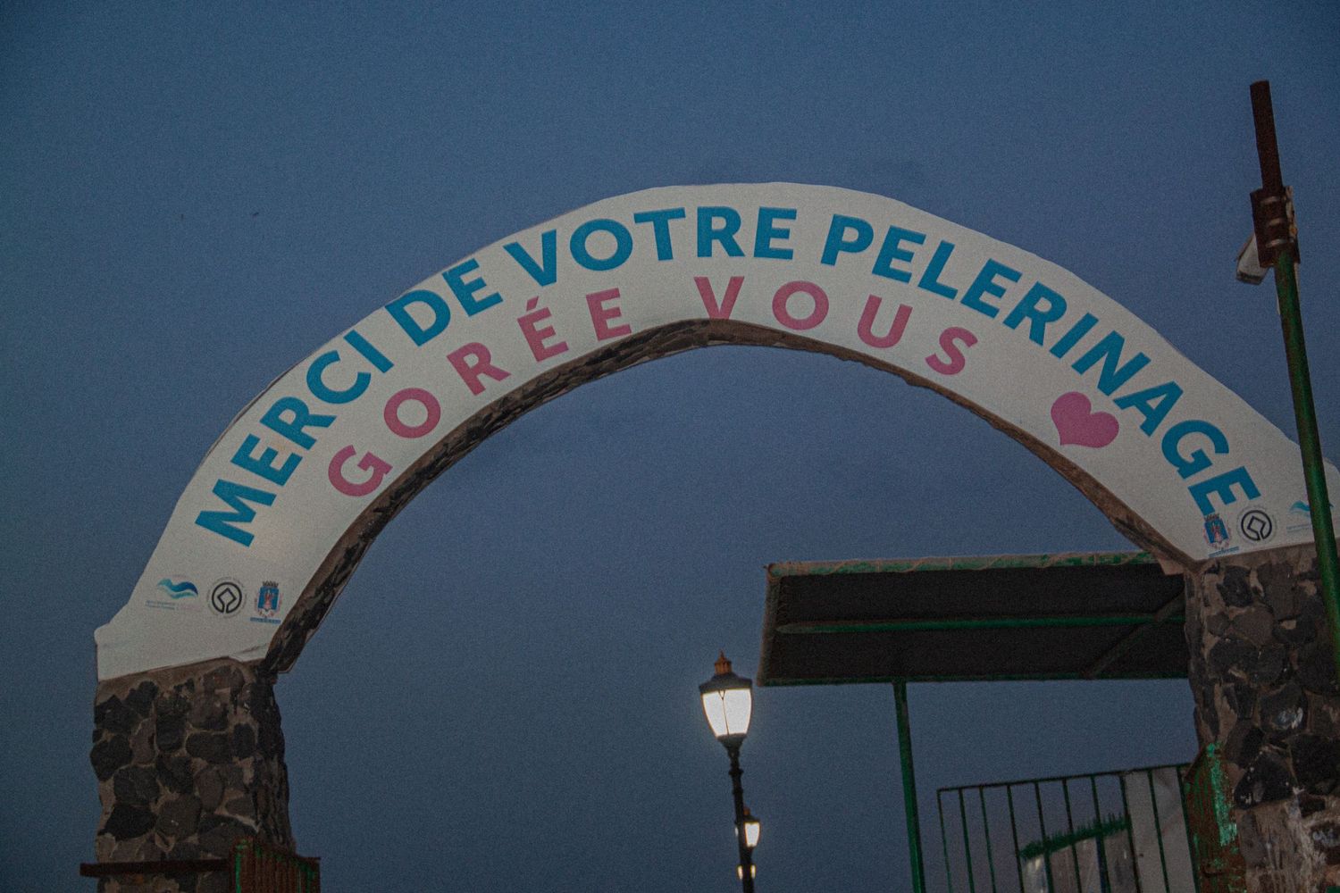 Illuminated arch sign reading Merci De Votre Pelerinage Goree Vous at dusk on Goree Island, Senegal.
